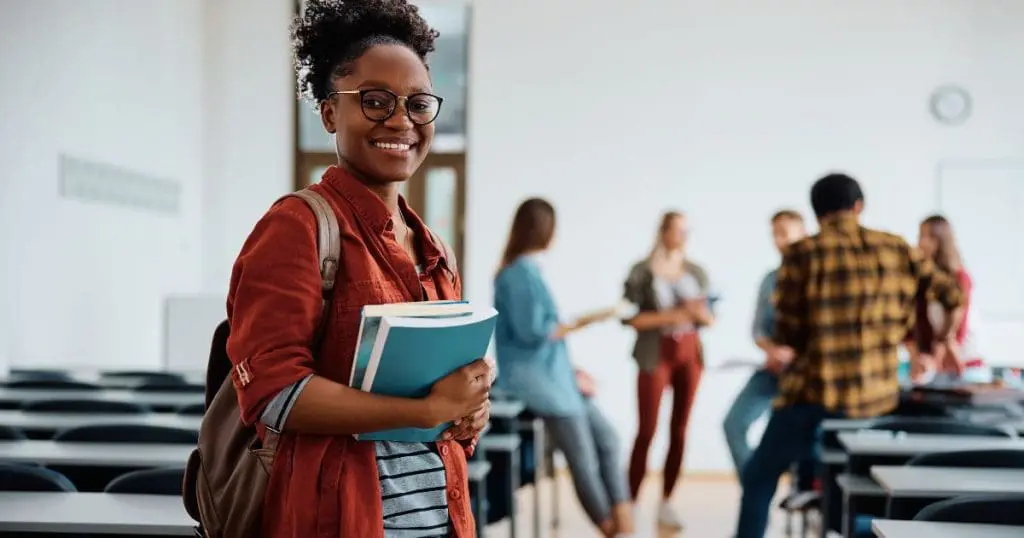 Cursos Rápidos - Aluna negra feliz na sala de aula olhando para a câmera.