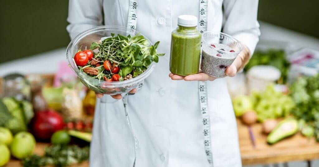 Mulher segurando legumes em frente a uma bela mesa repleta de alimentos - Técnico em Nutrição e Nutricionista