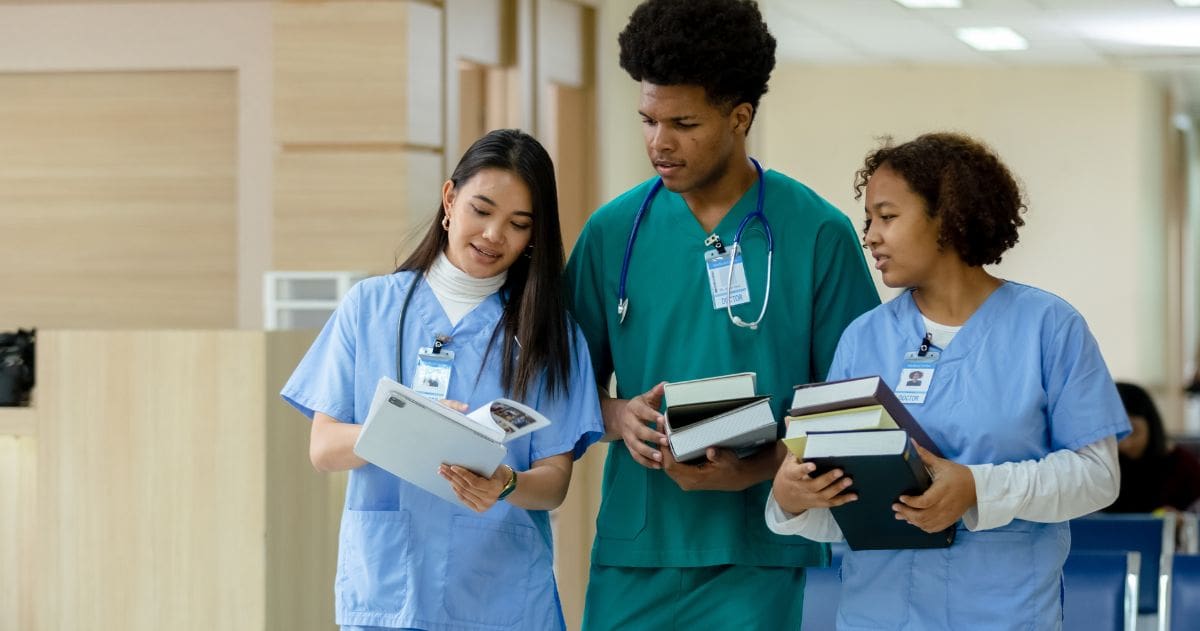 O que fazer depois da conclusão do Curso Técnico em Enfermagem? - grupo de estudantes de enfermagem segurando um livro andando e conversando na instituição de ensino.